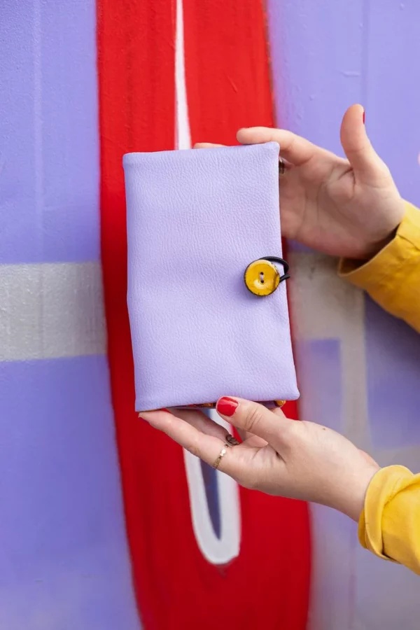 Portefeuille femme Tulipop mauve tenu à la main dans un univers coloré